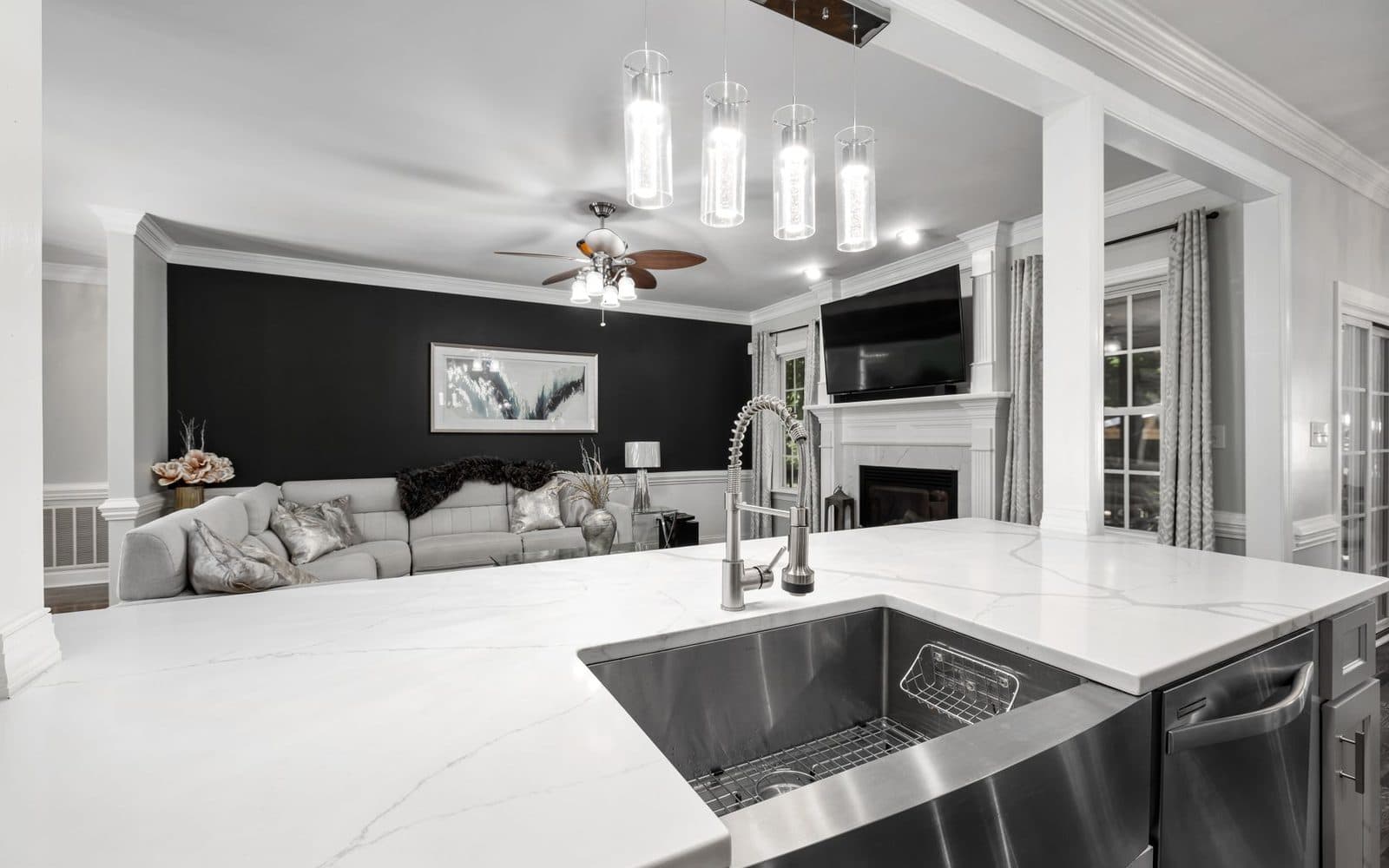 Large white stone kitchen island with a stainless steel sink and a chrome pull-down tap in a bright open-plan home