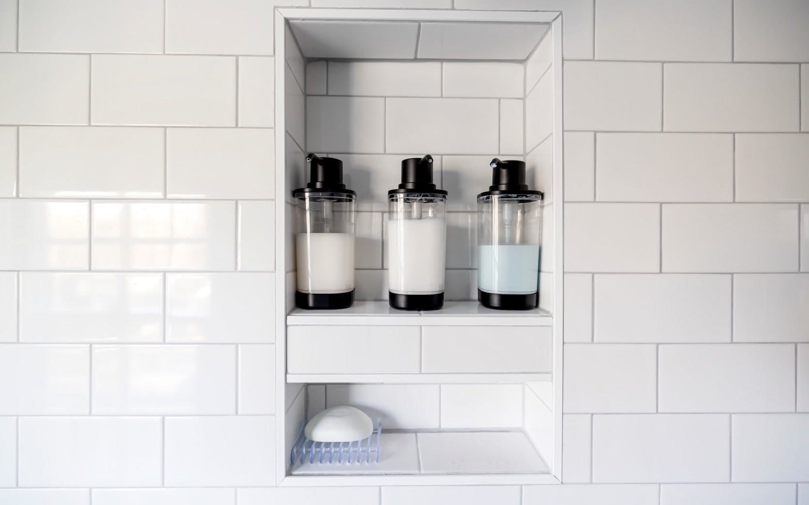 Clean white subway tiles and grout around a shower niche holding shampoo, conditioner and body wash dispensers