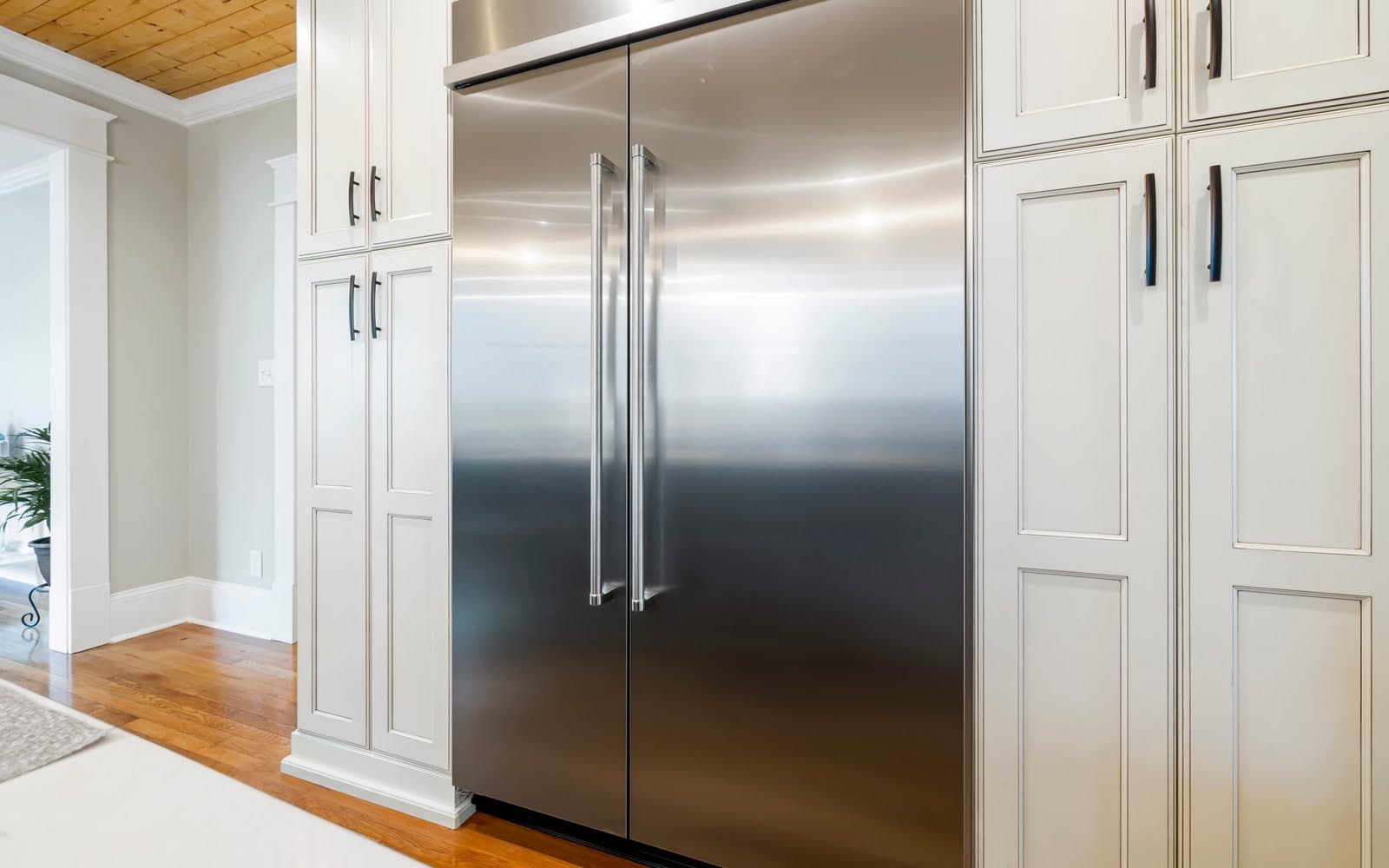 Streak-free built-in stainless steel fridge between white shaker cabinets in a large family kitchen