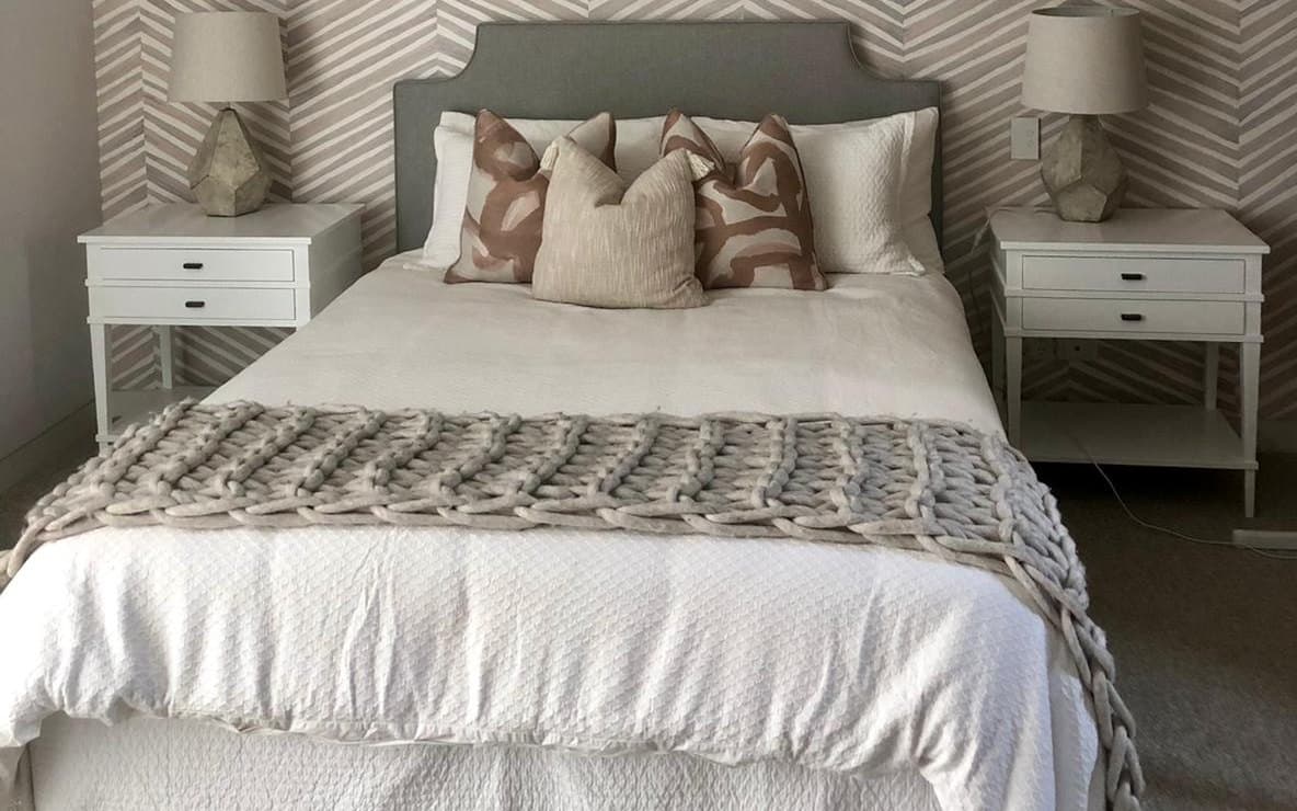 Freshly made bed with crisp white linen, a grey upholstered bedhead and a chunky knit throw in a calm, light-filled bedroom