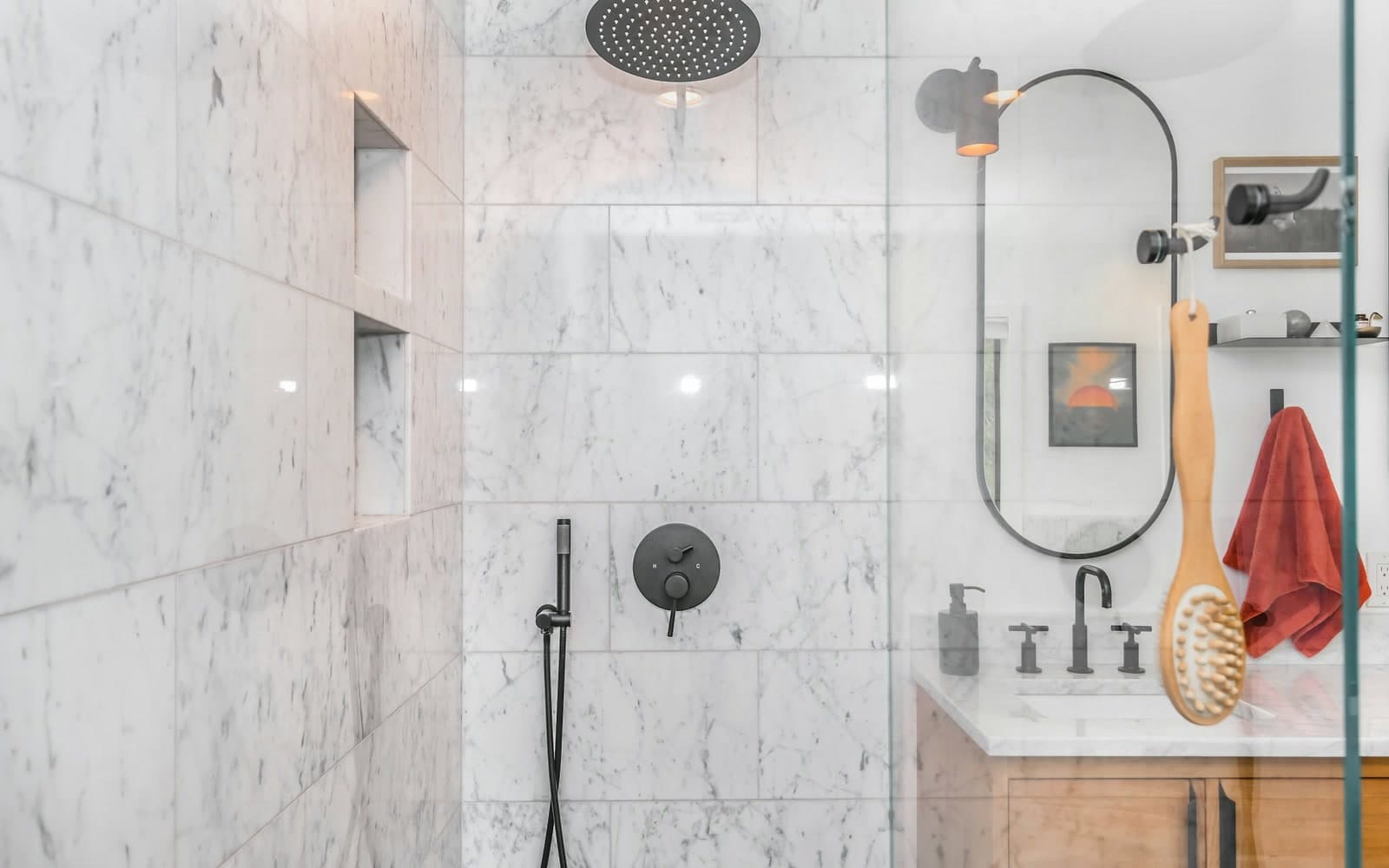 Clear frameless glass shower screen in a marble family bathroom, with a bath brush and towel hanging by the timber vanity