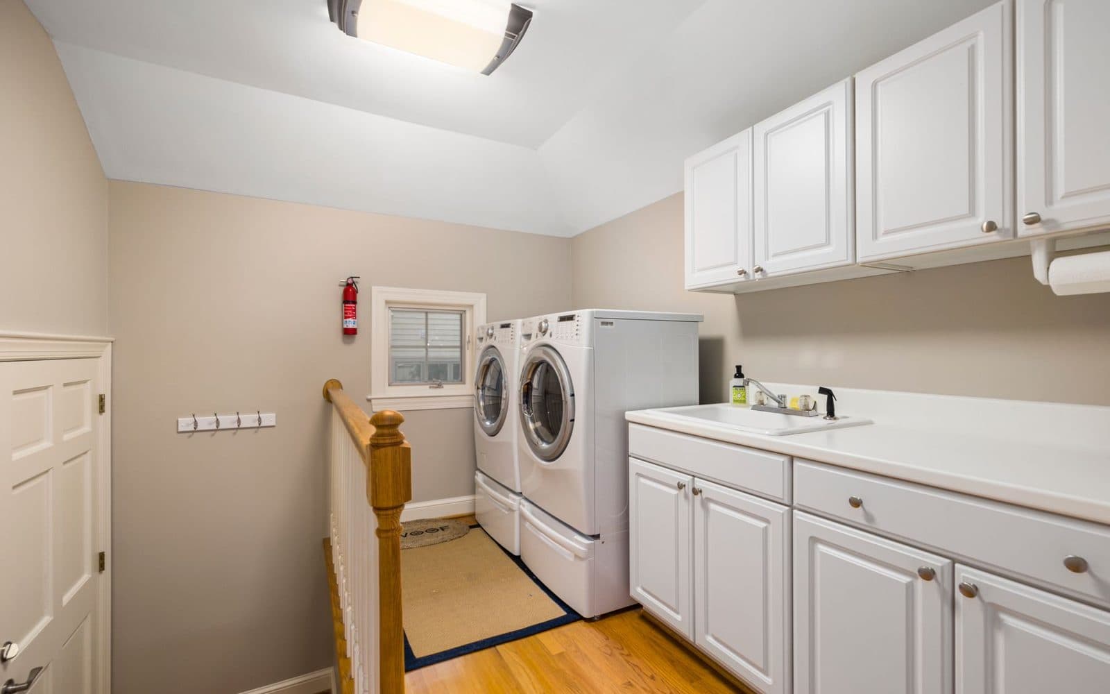 Bright, tidy laundry with white cabinets, a front-loading washer and dryer and timber floors